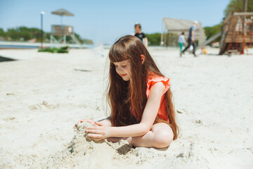 A 7-year-old girl plays in the sand on a city beach. Vacation and rest. Playful active child on the...