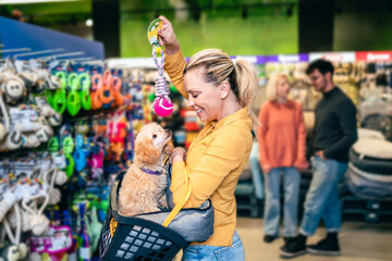 Beautiful middle aged blond woman buying accessories and food for her poodle puppy in pet shop. - 506220161