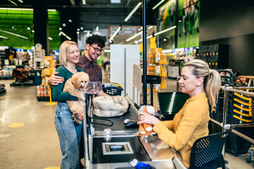 Happy young couple buying accessories and food for their poodle puppy in pet shop.