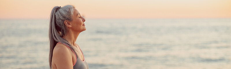 Close-up photo of sporty female sitting on the edge of shore with her eyes closed, relaxing