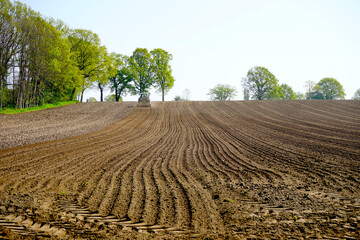 freshly plowed, slightly hilly field with tractor and plow at the end, farmland, landscape,...