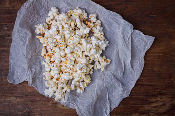 Heap of ready popcorn on white paper brown wooden table background. Top view