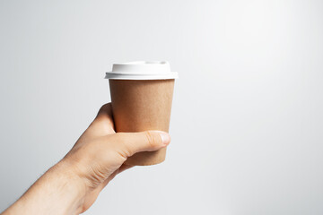 Close-up of male hand holding paper cup of coffee takeaway, on white background.
