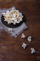 Heap of popcorn in black bowl on wooden rustic background. Some popcorns on fabric and table. Vertical shot