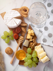Top view of a snack of cheese, nuts, honey and grapes, a glass of white wine, on a wooden plate in...