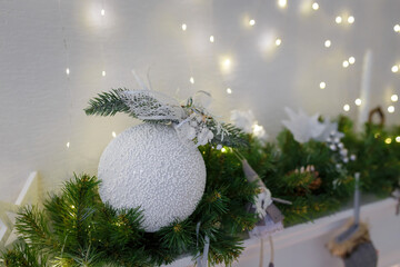 White bauble and fir branches on decorated fireplace top, wooden toys and garlanf lights. Merry Christmas, Happy New Year