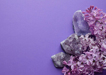 Beautiful lilac flowers and semi-precious amethyst druze lie on a purple background. Copy space.