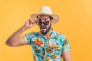 Latin man wearing summer clothes, hat and modern sunglasses looking surprisingly to the side over orange background, studio shot. High quality photo