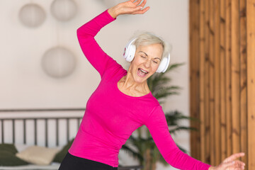 Beautiful senior woman with short grey hair and lovely smile listening to music and dancing at home . Concept of attractive good looking elderly female, mature women with active lifestyle.