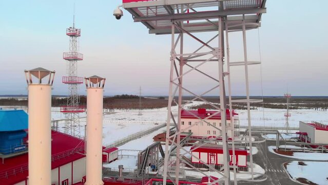 A drone flies near a metal tower for plant lighting in winter, a petrochemical plant aerial view of the plant and lightning rod towers protecting equipment. Fuel crisis in winter.
