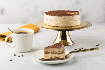 Tiramisu cake on a golden cake stand. Light background