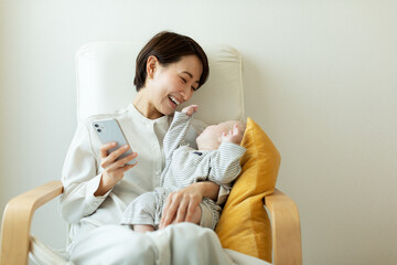 赤ちゃんを抱っこしながら携帯電話を操作する母親