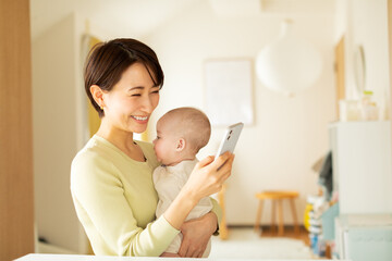 赤ちゃんを抱っこしながら携帯電話を操作する母親