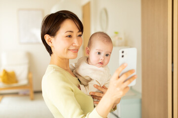 Obraz na płótnie Canvas 赤ちゃんを抱っこしながら携帯電話を操作する母親