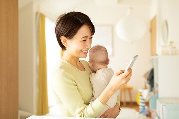 赤ちゃんを抱っこしながら携帯電話を操作する母親