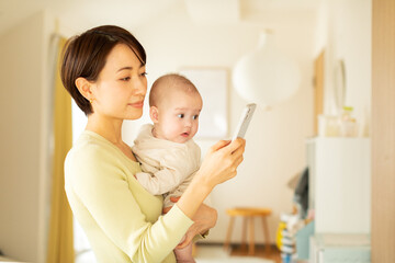 赤ちゃんを抱っこしながら携帯電話を操作する母親