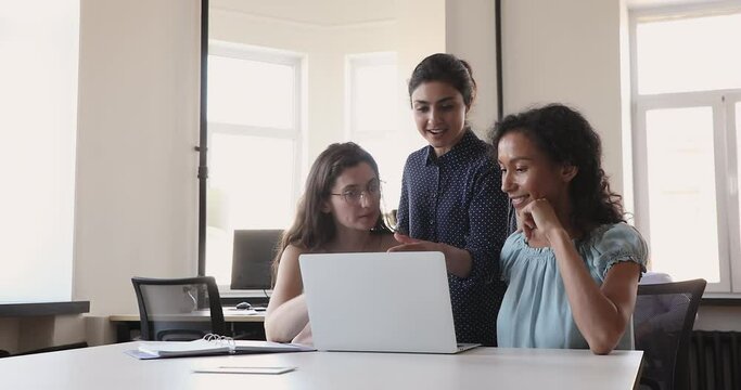 Indian woman mentor leader teach multiethnic female group of interns explain work coaching newbies in doing online job on laptop. Three young multiethnic business ladies coworking on project together