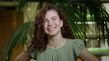 Close-up of a young very cheerful woman with brown, curly hair looking into the camera. Portrait of a girl