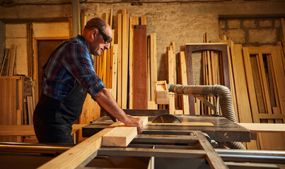 Wood cutting table with electric circular saw.  Senior Professional carpenter in uniform cutting wooden board at sawmill carpentry manufacturing . Sawing machine