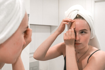 Beauty concept. Wellness, taking care  yourself. Portrait beautiful woman looking in the mirror in the bathroom.Beautiful girl bath towel  her head, taking care of herself, gouache massage, mask, spa