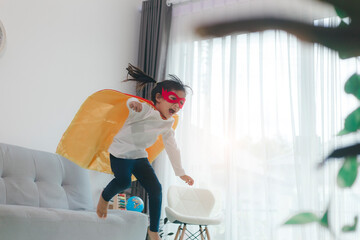 Girls child jumping on home living room couch wearing improvised superhero outfit fancy dress,...
