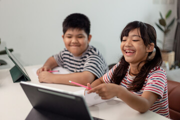 Fototapeta na wymiar Asian boys and girls enjoy online learning by taking notes and using tablets at home.