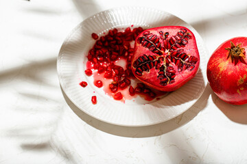 A pomegranate cut in half and whole lies on a table covered with a white tablecloth. 