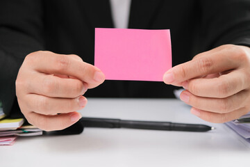 Close-up of business woman hands holding blank pink note paper with copy space at work. Office supplies and text with copy space template concept