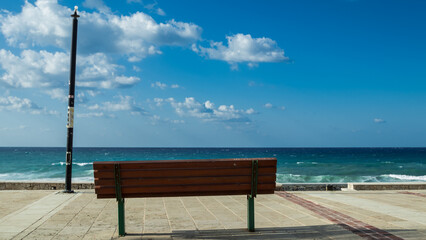 Fototapeta na wymiar A wooden bench against the backdrop of blue cloudy sky and sea. 