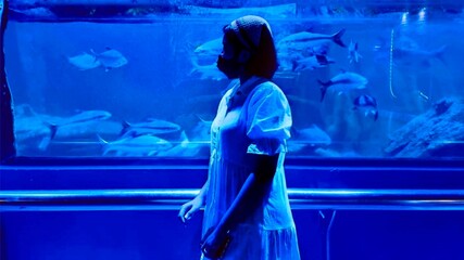 Woman  watching the shoal of fish swimming in aquarium.