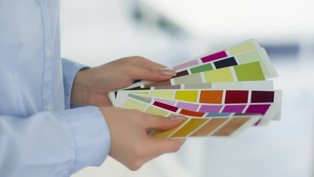 Close up shot of unrecognizable woman designer choosing color for project, hands mixing color swatches at office