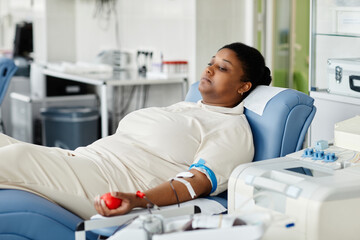 Portrait of young African American woman giving blood while laying in chair at plasma donation...