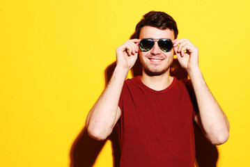 Lifestyle, fashion and people concept: Portrait of a young handsome man wearing sunglasses on yellow background