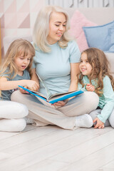 Happy blond mother reading a book to her cute daughters sitting on the floor