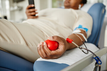 Close up of young black woman squeezing stress ball while giving blood at donation center, copy space