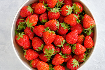 Juicy, bright and sweet strawberries in a bowl on a white concrete table