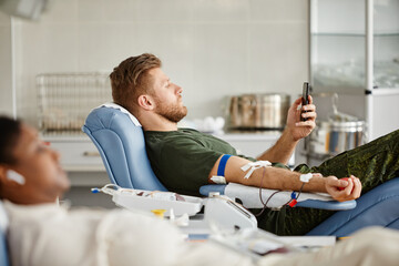 Side view portrait of military man giving blood while laying in chair at blood donation center and...