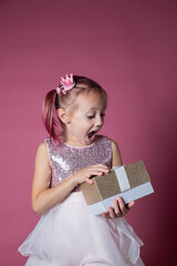 Little caucasian girl in a festive dress with sequins posing opening gift box