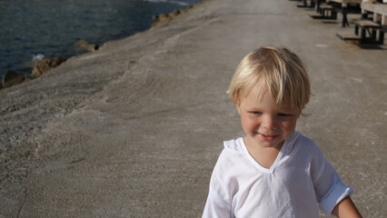 little boy in a white shirt by the sea running towards the camera