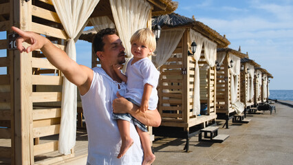 dad holds his son in his arms and shows him something with a finger in white shirts