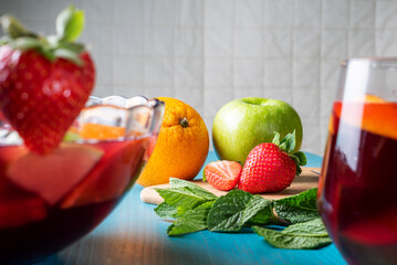 Orange, apple, strawberries and mint, some of the ingredients of the sangria, with a glass and a bowl of sangria in the foreground out of focus.