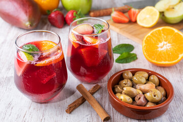 Two glasses with sangria, a typical Spanish drink, accompanied by some olives. In the background, some of the fruits used in its preparation.
