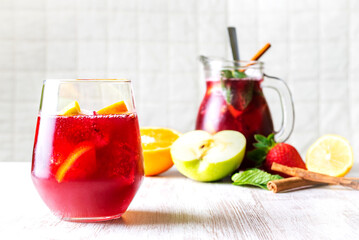 Glass with fresh sangria in the foreground, a typical Spanish drink, with a jar in the background out of focus, various fruits, mint and cinnamon.