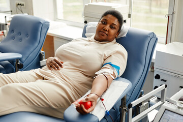 Portrait of young black woman donating blood in comfortable chair and looking at camera, copy space