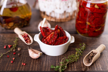 Sun-dried tomatoes in olive oil in a white bowl with pepper, garlic and thyme in a rustic style. Selective focus, close-up.