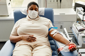 Portrait of young black woman donating blood while lying in chair and wearing mask, copy space