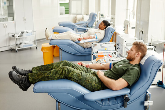 Group of blood donors in row laying on med chairs in donation center - Powered by Adobe