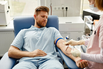 Portrait of handsome young man preparing for blood donation at med center with nurse helping - obrazy, fototapety, plakaty