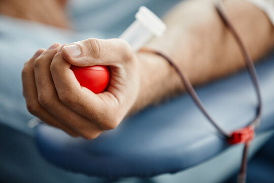 Close up of young man donating blood and holding red ball in hand, copy space