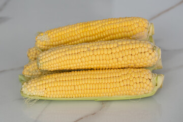 many gold ear of corns vegetable on a white marble background